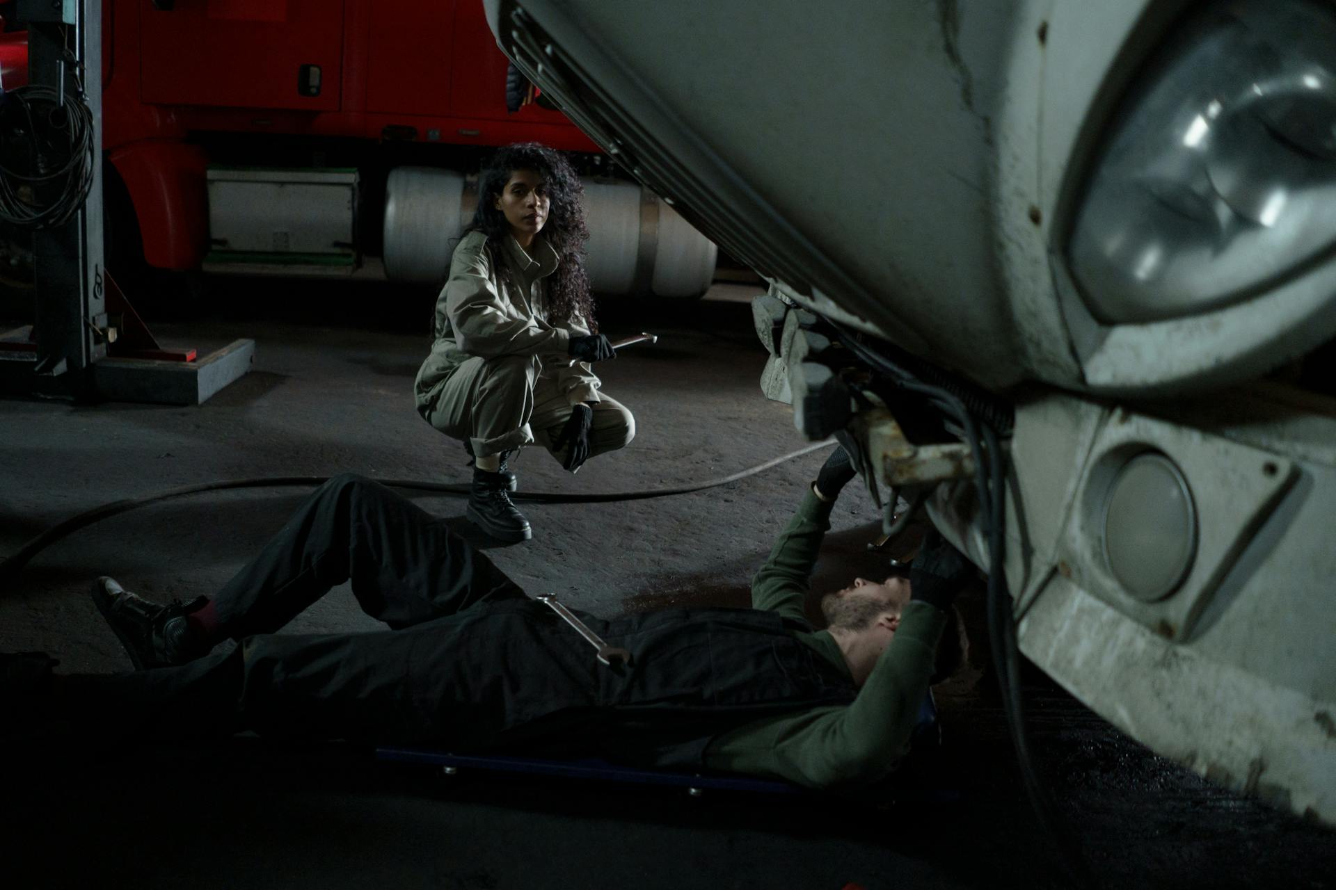Two mechanics performing maintenance on a truck inside a garage setting.