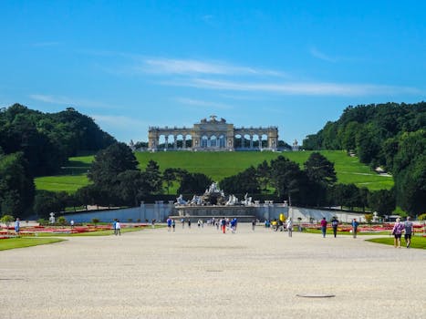 People walking in Schönbrunn Palace Gardens towards the Gloriette in Vienna on a sunny day.