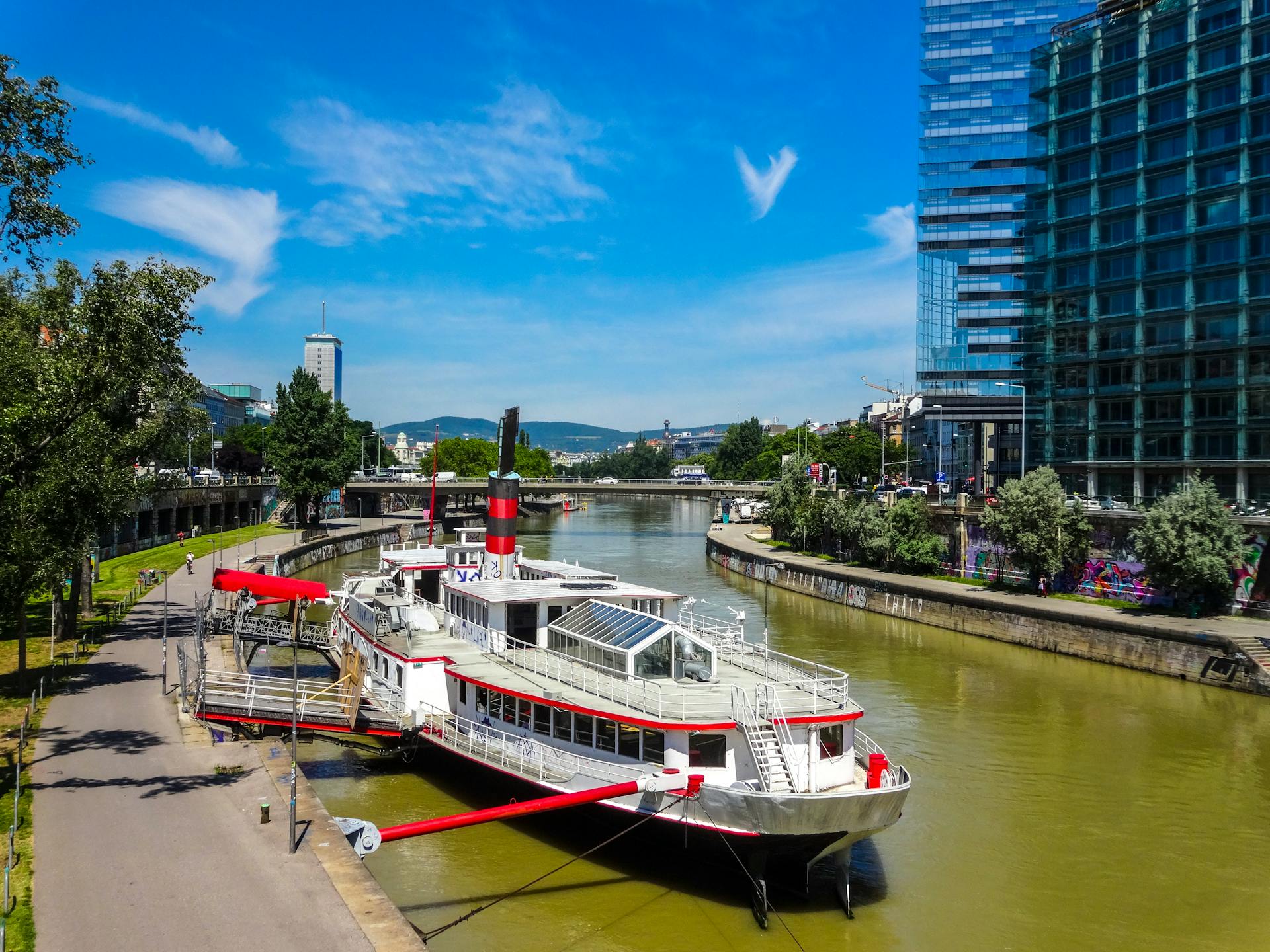 A modern boat docked on the Danube Canal in Vienna, Austria with urban cityscape.