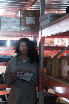 Woman in uniform holding clipboard while managing warehouse inventory.