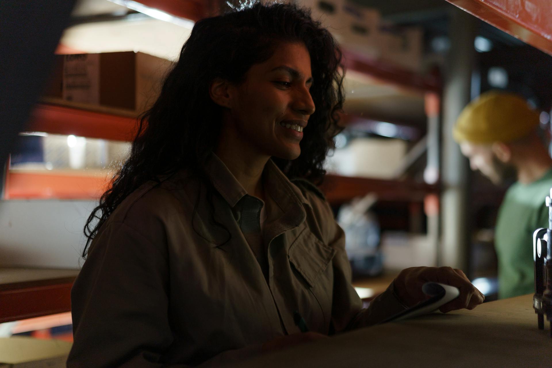 Smiling female worker examines inventory in a dimly lit warehouse.