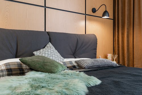 Interior of bedroom with cushions placed on soft bed under lamp hanging above bedside with aroma sticks