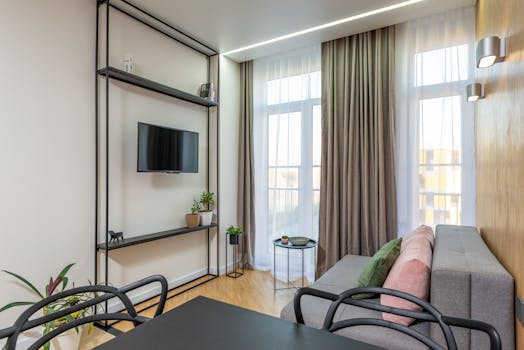 Stylish living room with contemporary decor, featuring a sofa, TV, plants, and elegant curtains.
