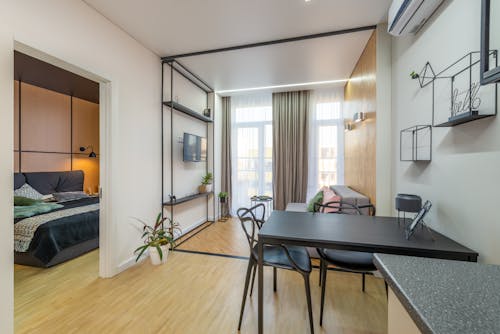 Black table with chairs placed near living room with couch and TV in spacious light apartment with bed in bedroom