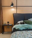 Comfortable bed with pillows and soft blanket placed at wooden wall near bedside table in modern light bedroom at home