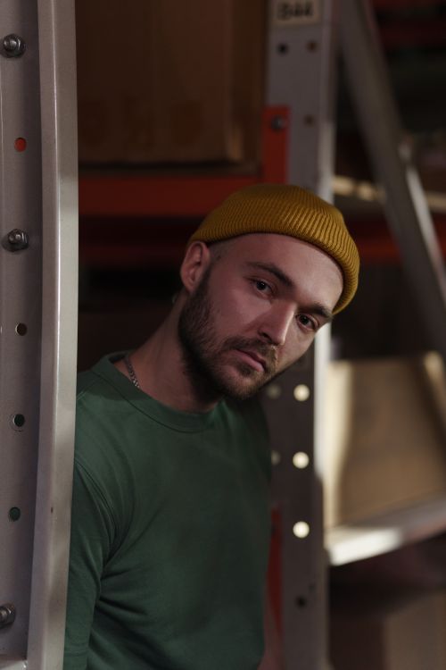 Free Close-up portrait of a young man wearing a yellow beanie and green shirt indoors. Stock Photo