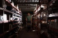 Man in Green Polo Shirt Standing Near Brown Wooden Shelf
