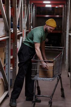 A man in a green shirt and hat organizes boxes in a warehouse, showcasing efficient storage work.