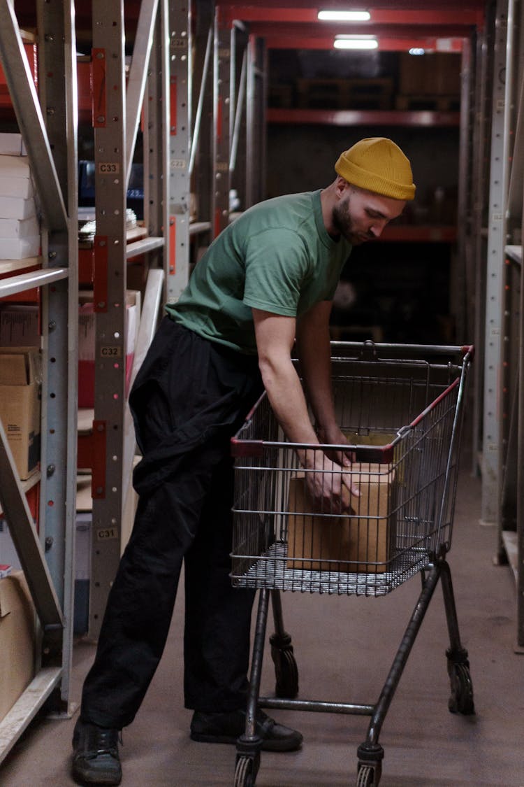 Man In Green Shirt And Black Pants Holding A Box On Shopping Cart