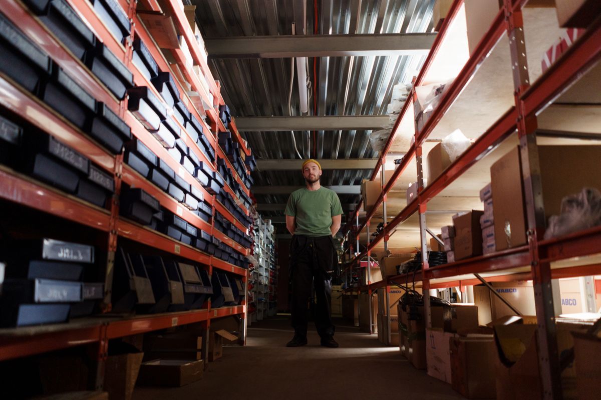 A man standing in a warehouse aisle surrounded by shelves filled with boxes and inventory.