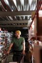 Man in Green Crew Neck T-shirt and Yellow Cap Standing Near Brown Wooden Shelf