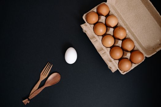 Brown eggs in carton with single white egg on dark background. Minimalist food concept.