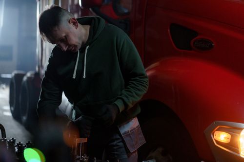 Free A male mechanic works on a truck engine inside a dimly lit garage, emphasizing skill and industry. Stock Photo