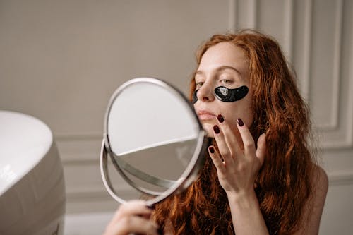 A Woman With Under Eye Masks Looking at a Mirror 