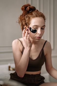 A woman applies an eye mask while practicing her skincare regimen in a serene setting.