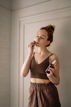 A woman practices self-care using a jade roller and skincare products indoors.