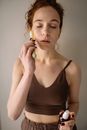 A Woman in Brown Tank Top Massaging Face with a Jade Roller