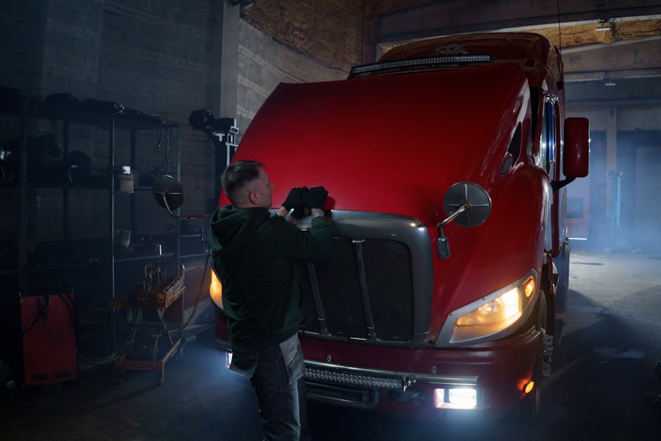 What is a truck driver? Mikä on rekkakuski? - Mechanic wearing gloves working on red truck hood in dimly lit garage.