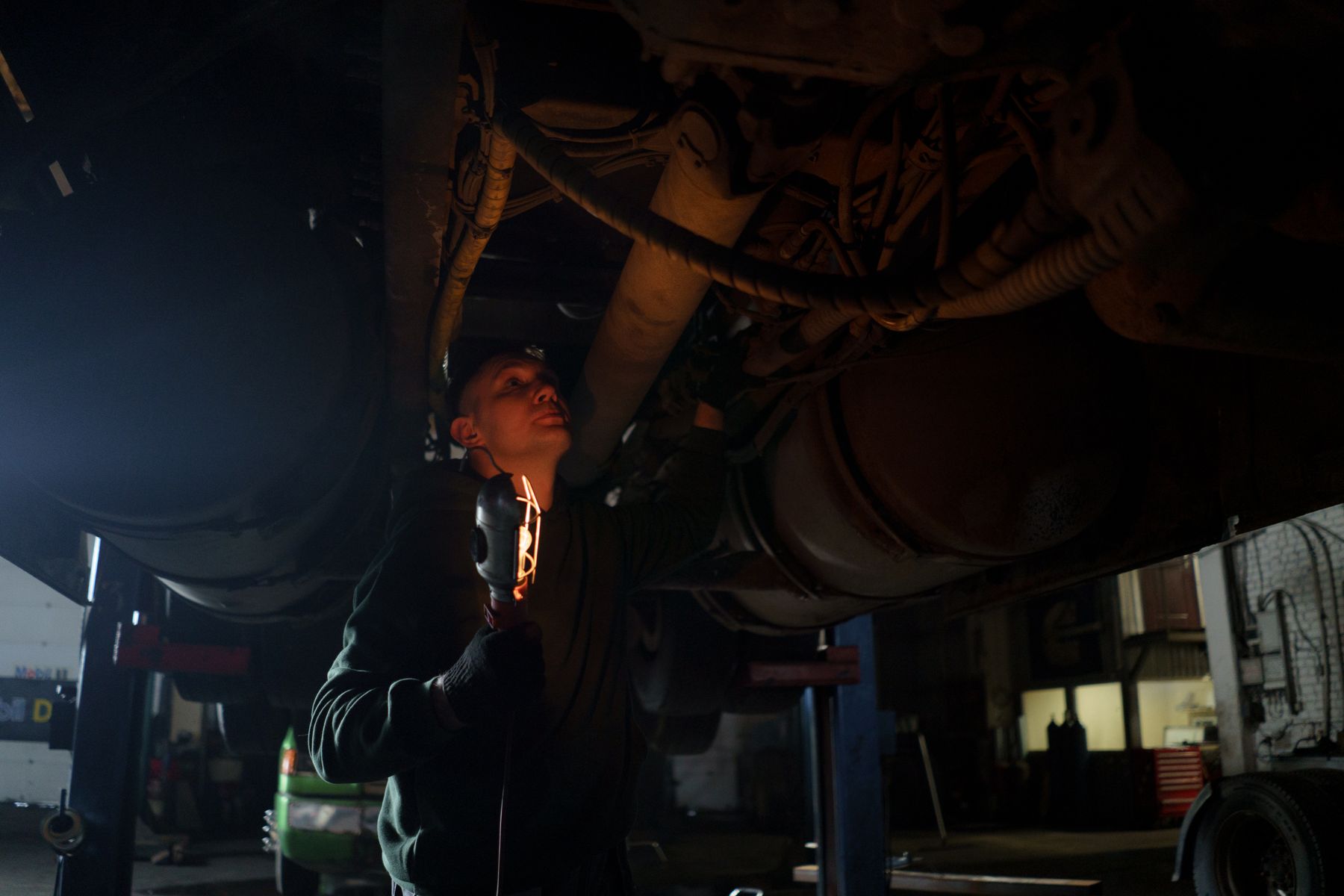 Mechanic holding an inspection light while examining the underside of a raised vehicle.