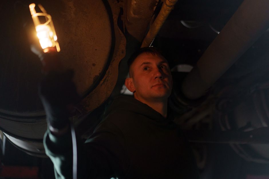 Auto mechanic inspecting undercarriage with handheld lamp, ensuring vehicle safety.