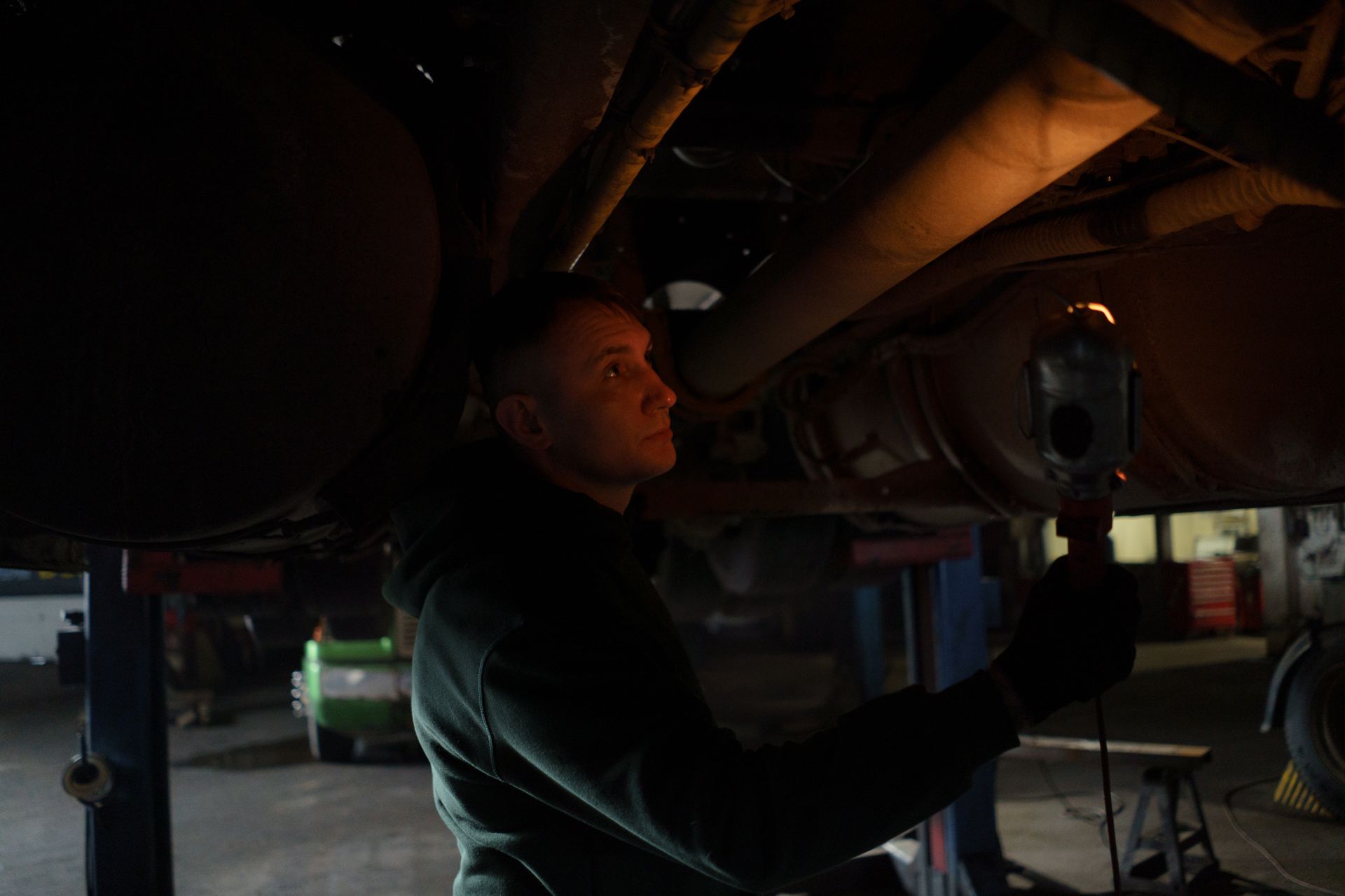 Mechaniker kontrolliert mit einer Lampe den Unterboden eines Fahrzeugs.