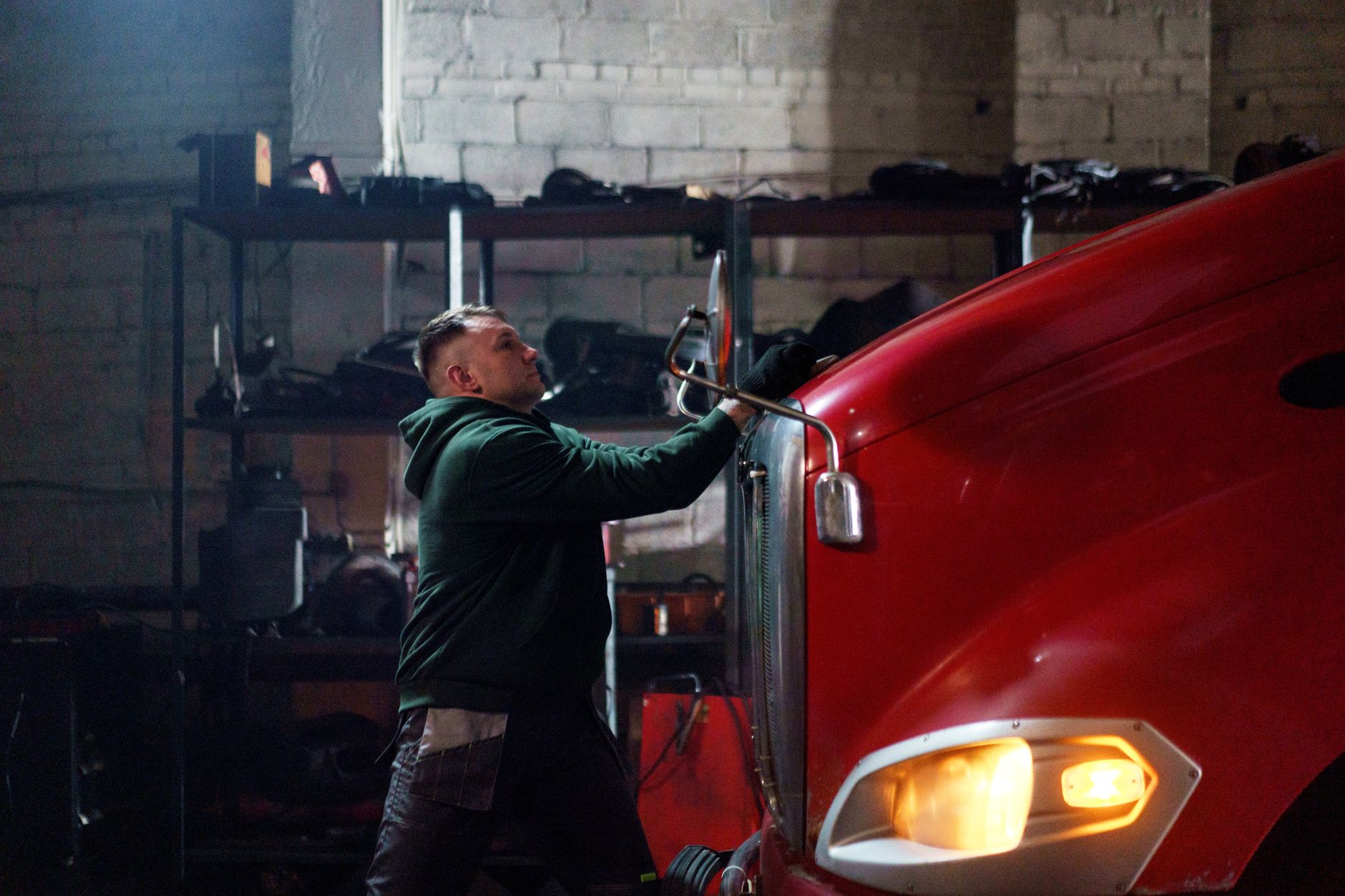 Mechanic working on a red truck in a dimly lit garage.