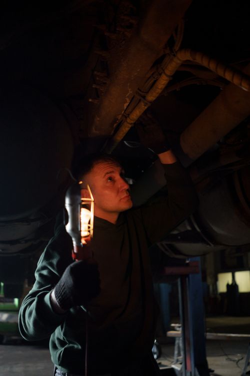 Free Automotive mechanic using handheld light to inspect a vehicle's underbody in a repair shop. Stock Photo