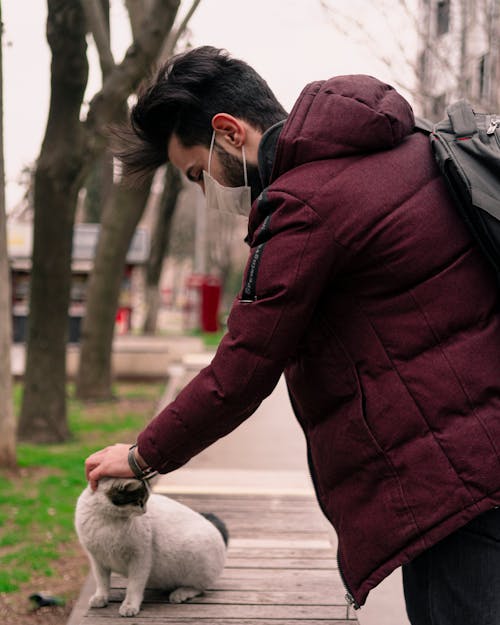 Free Man in a Red Jacket Petting a Cat Stock Photo