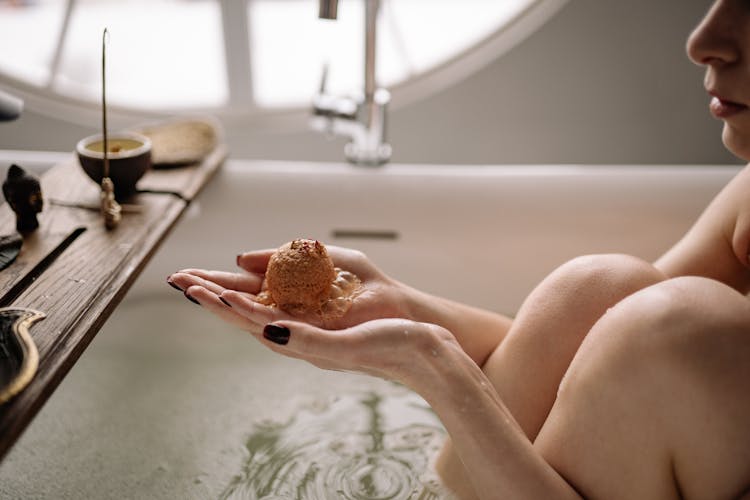 A Person In A Bathtub Holding A Melting Bath Bomb