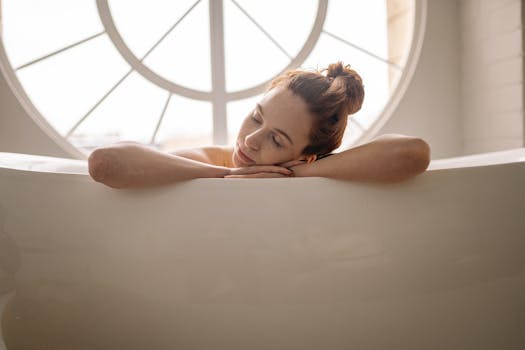 A woman peacefully rests in a bathtub by a circular window, capturing a tranquil indoor setting.