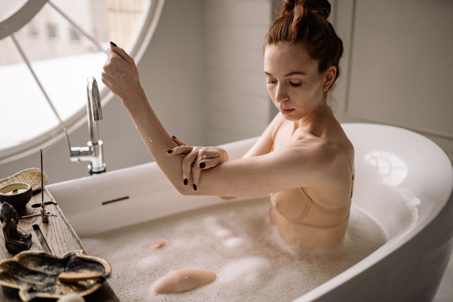 A serene scene of a woman indulging in a calming bubble bath with natural light and soothing ambiance.