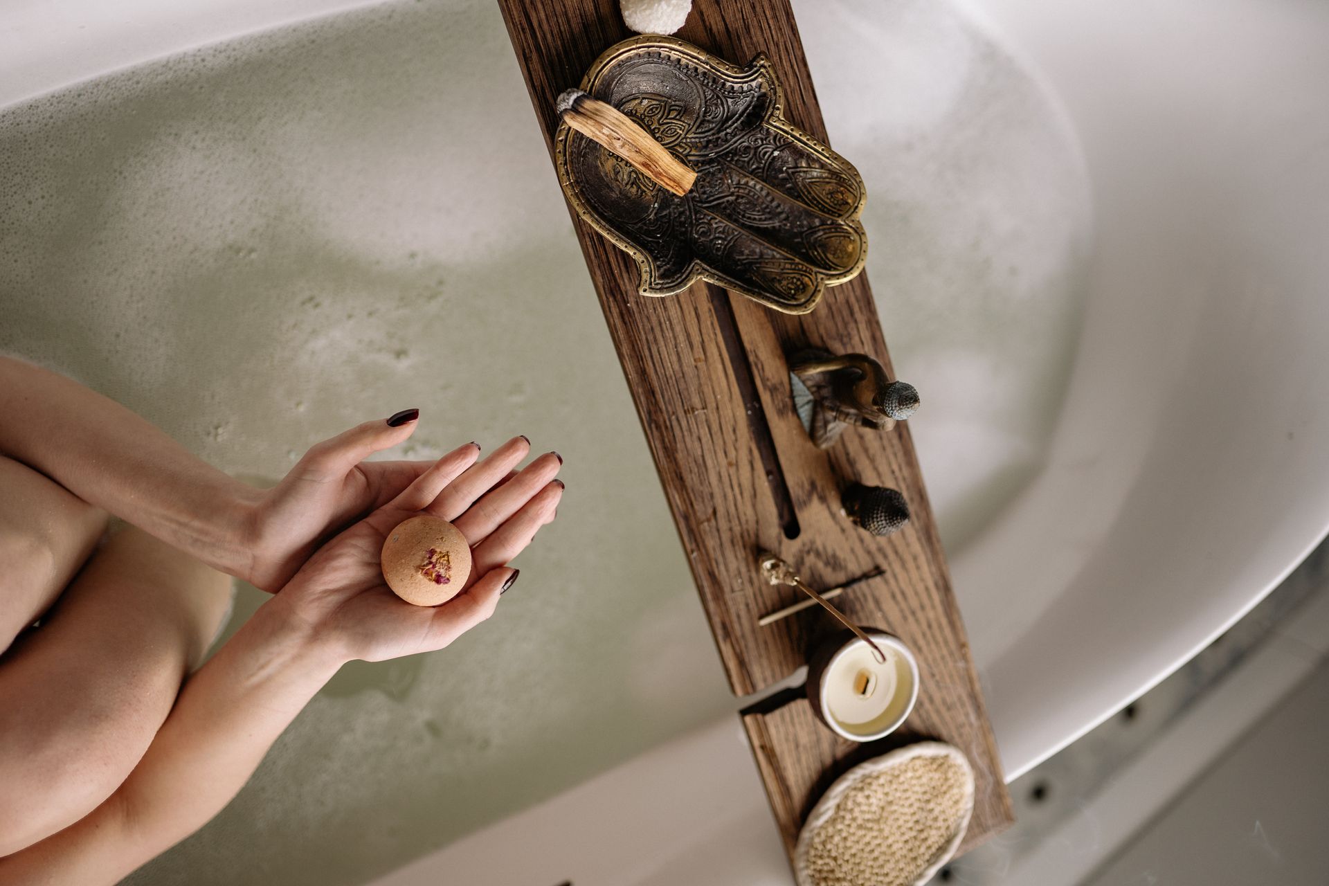 A Person in a Bathtub Holding a Bath Bomb Near a Wooden Plank with Palo Santo