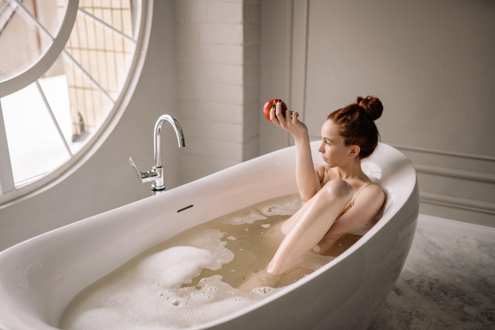 A redheaded woman enjoys a relaxing bath while holding an apple, conveying self-care and tranquility.