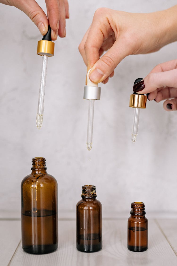 People Holding Dropper Caps Above Clear Glass Bottles