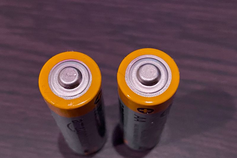 Top view of two AA batteries with yellow tops on a dark surface.