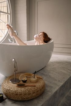 A serene moment in a bathtub as a redheaded woman enjoys beauty rituals, emphasizing relaxation.