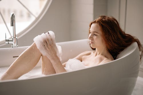 Photo of a Topless Woman with Red Hair Taking a Bath