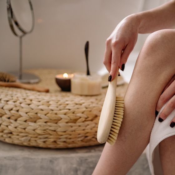 A dry body brush being used beside a lit candle and woven mat. Photo by Yan Krukau on Pexels.