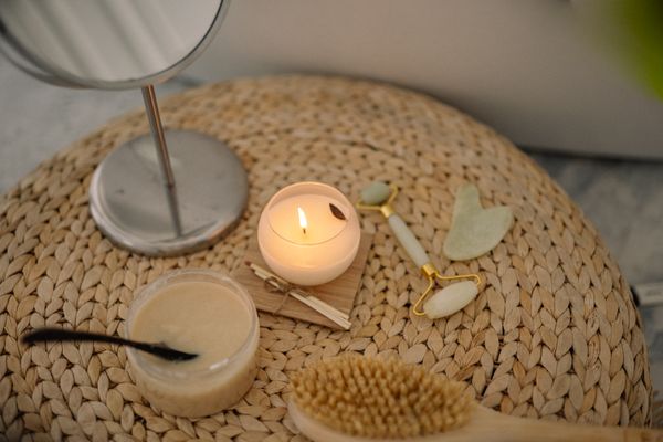 Candle, jade roller and body scrub arranged on a woven mat