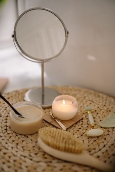 A calming spa scene with a lit candle, mirror, brush, and jade roller on a woven mat.