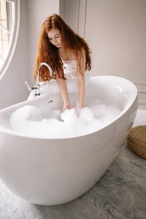 Free Photo of a Woman with Red Hair Touching the Bubbles in a Bathtub Stock Photo