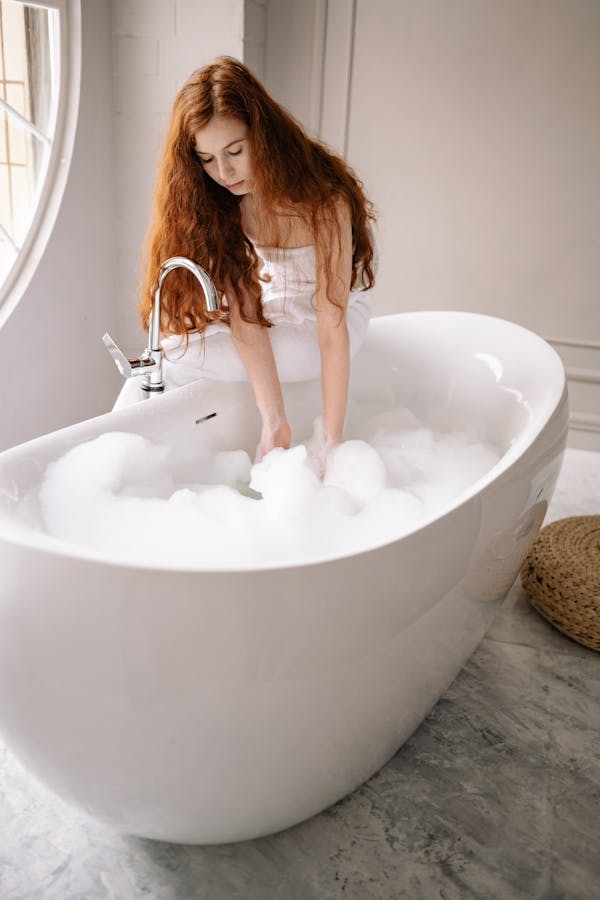 Photo of a Woman with Red Hair Touching the Bubbles in a Bathtub
