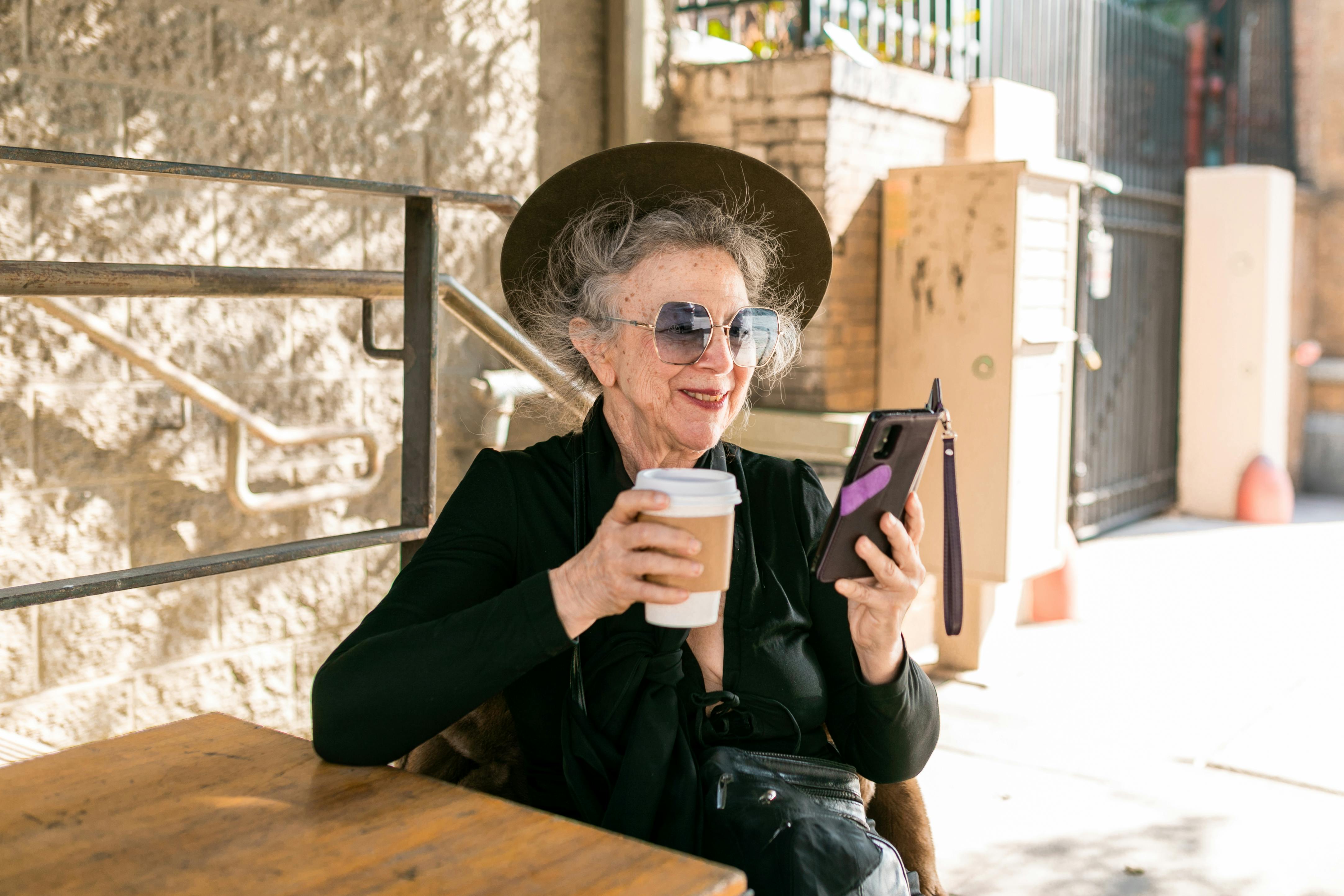 Woman in black using her mobile phone while having coffee. | Photo: Pexels