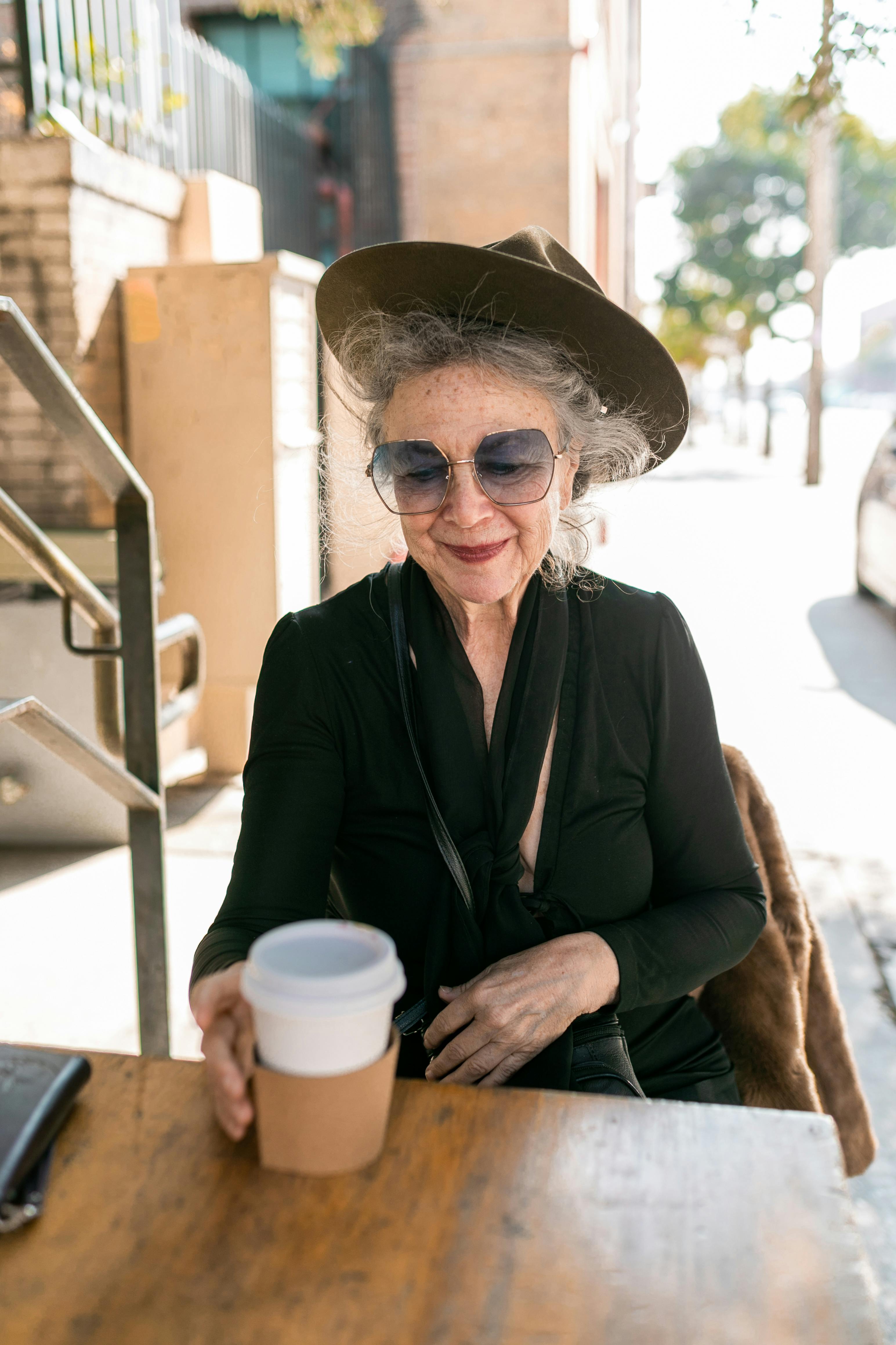 woman in black coat and brown hat holding white disposable cup