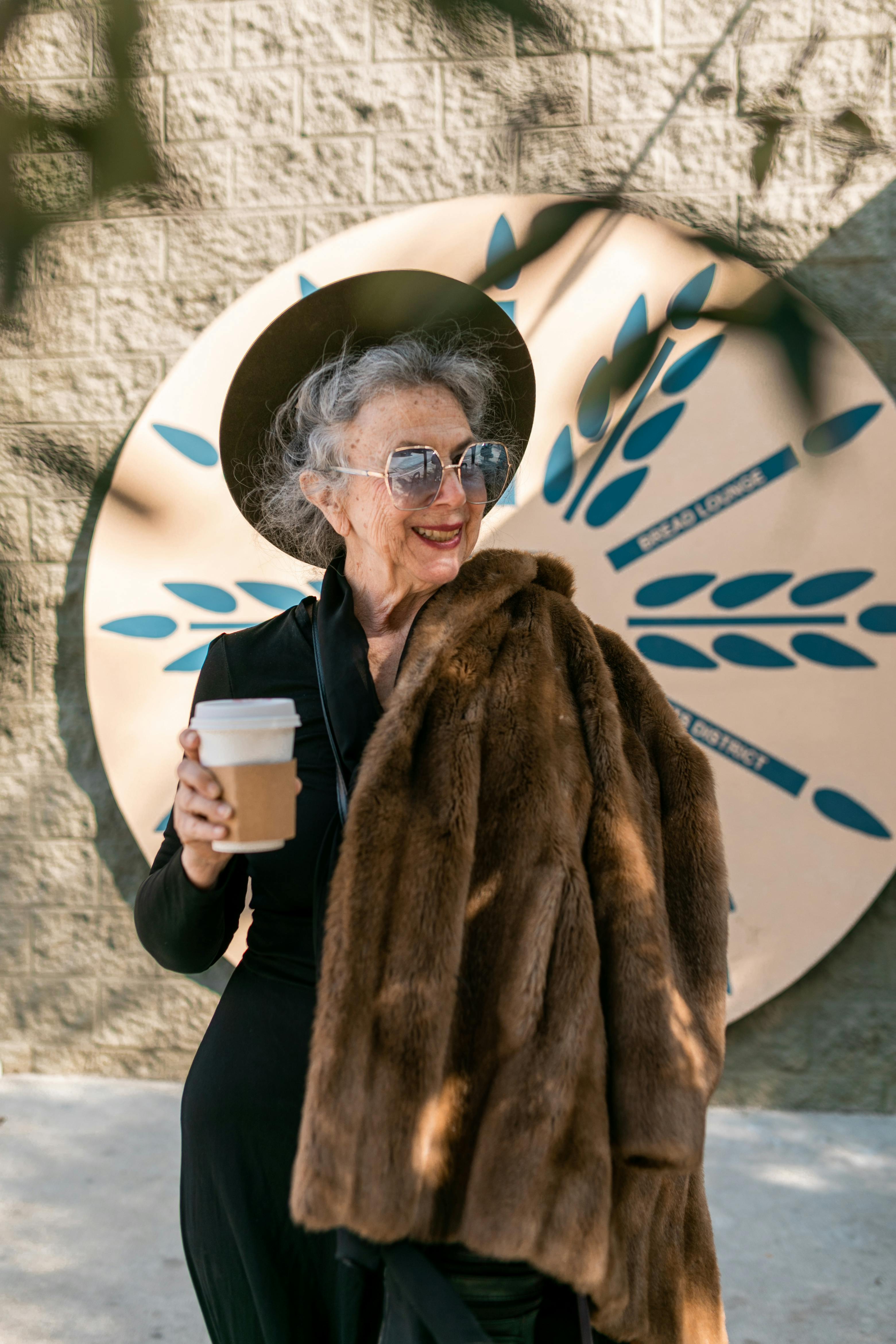 woman in brown fur coat holding white coffee cup