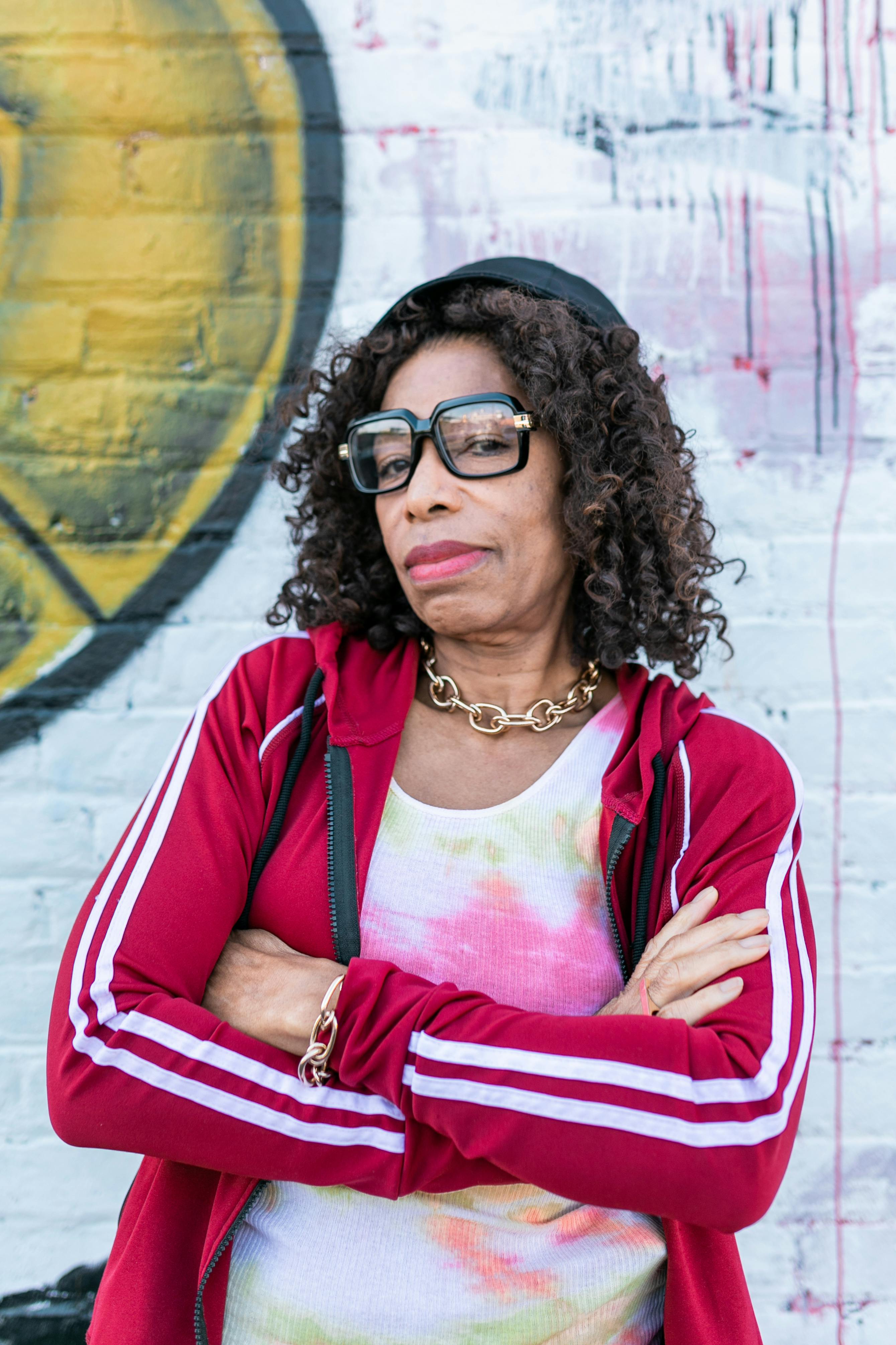 Confident senior woman with curly hair and glasses posing against a graffiti wall. Urban fashion style.