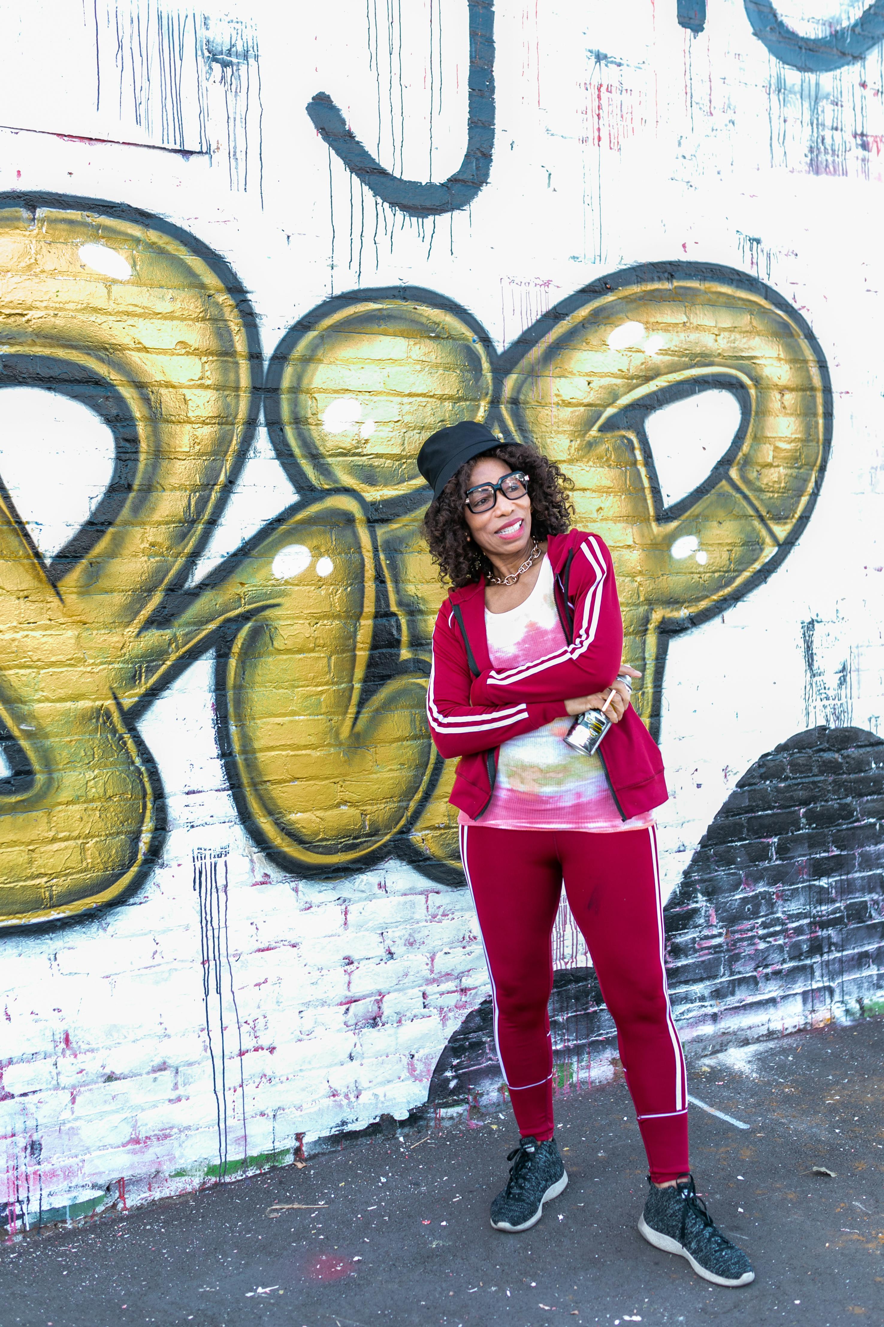 woman in red and white long sleeve jacket and red pants standing beside a wall with graffiti