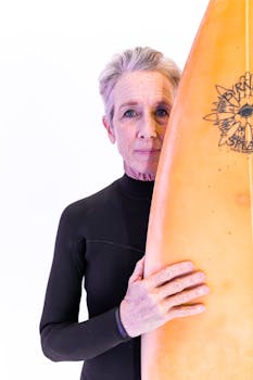 Elderly woman wearing a wetsuit and holding a surfboard, embracing active lifestyle.