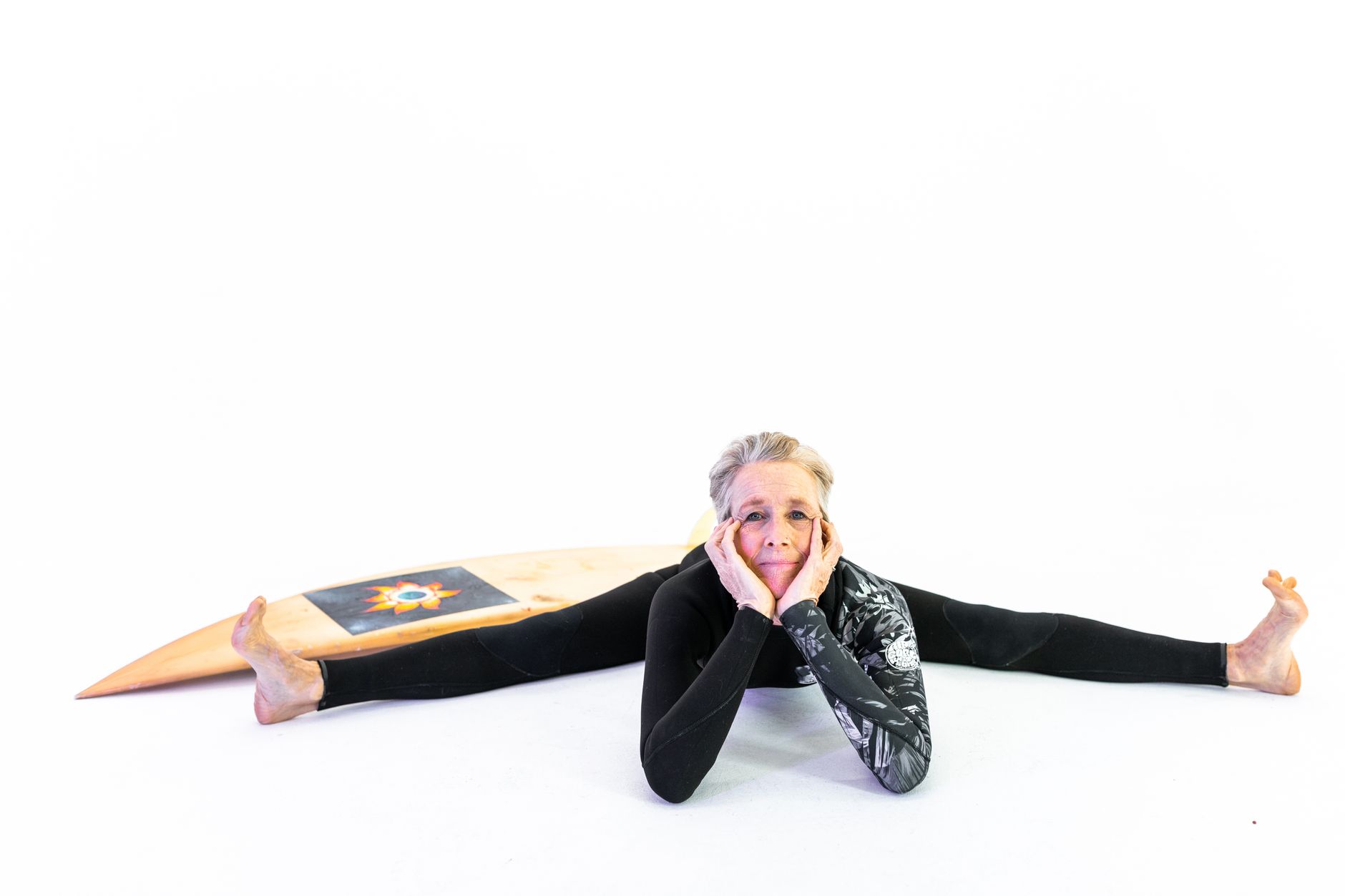 健身如何幫助更年期女性緩解症狀並提升活力 Cheerful senior woman in activewear stretching with a surfboard indoors, embracing vitality and wellness.