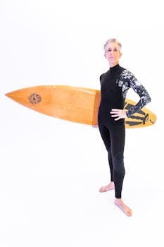 Confident senior woman in wetsuit holding a surfboard, embodying active and healthy living.